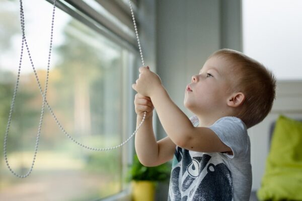 A child playing with a blinds cord at a window.